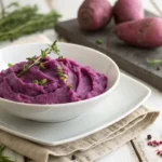 Mashed purple sweet potatoes in a white bowl with herbs.