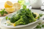 Steamed broccoli with lemon wedges on a white plate.